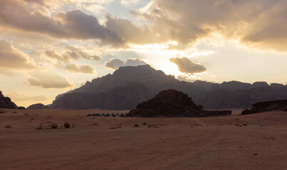 Wall Mural - Panoramic sunset view of Wadi Rum desert in Jordan with clouds moving over flat sand landscape with mountains in background, 