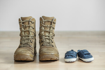 old worn military boots and baby shoes on wooden floor. Concept of military father and family.