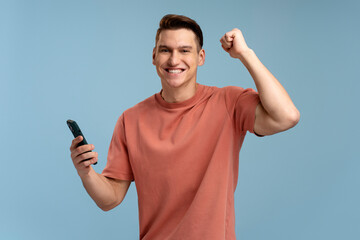 Happy satisfied man in t shirt holding smartphone and smiling making yes gesture