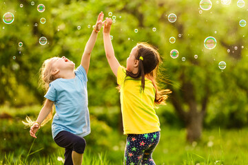 Two little girls are blowing soap bubbles, outdoor shoot.