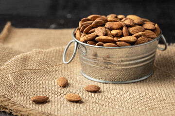 Wall Mural - Metal bowl full of almonds on a sackcloth. Pile of nuts stacked together randomly on the burlap background. Healthy nutrition concept
