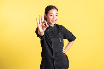 asian female chef smiling with okay hand gesture standing on isolated background