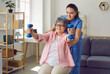 © Studio Romantic - Smiling senior woman lifting dumbbells, therapist assisting her. Cheerful female nurse helping elderly patient to do physical exercise at home. Disabled, elderly people rehabilitation and support