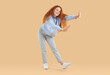 © Studio Romantic - Happy pretty woman dancing in studio. Full length shot of smiling young woman or teenage girl with long curly ginger hair wearing light blue jeans and sweatshirt dancing on beige studio background