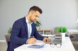 © Studio Romantic - Serious male financial director of business company is engaged in budget analysis and calculations. Side view of man at his workplace working with laptop, paper documents and calculator.