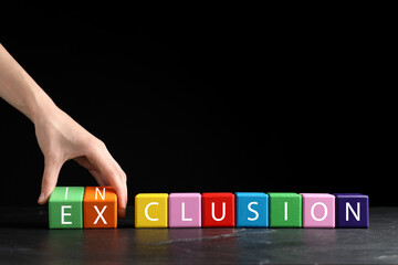 Wall Mural - Woman making word Inclusion with colorful cubes on marble table against black background, closeup. Space for text