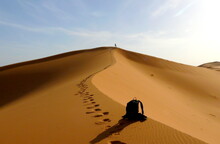 Detail Of Bag And Hiker Climbing To The Top Of The Great Sand Dune In The Red Dune Sea Of Erg Chebbi, Morocco.