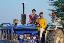 Indian Farmer Sitting With Wife And Daughter On Tractor At Field.