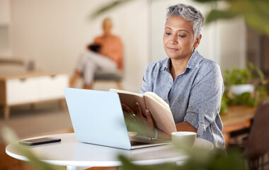 Laptop, book and senior woman reading while doing research for a project in the modern office. Technology, coffee and mature female marketing professional enjoying a novel story in her workplace.