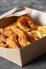 Wall Mural - Breaded fried chicken breast with fries and onion rings, in a cardboard tray with wooden cutlery. Environmentally friendly disposable plastic free container