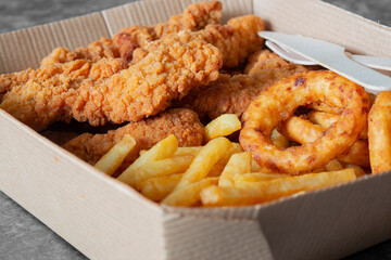 Wall Mural - Breaded fried chicken breast with fries and onion rings, in a cardboard tray with wooden cutlery. Environmentally friendly disposable plastic free container