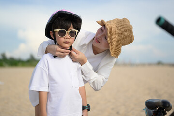 Wall Mural - Family on beach vacation, Young mother wearing safety helmet to cheerful boy before riding bicycle, Family with beach travel