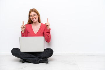 Wall Mural - Young redhead woman with a laptop sitting on the floor isolated on white background pointing up a great idea