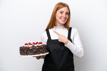 Wall Mural - Young redhead woman holding birthday cake isolated on white background pointing to the side to present a product