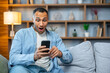 © Ivan - Emotional young bearded  man looking at cellphone screen, celebrating winning mobile game or getting price in online lottery, reading message with unbelievable pleasant news, good luck concept.