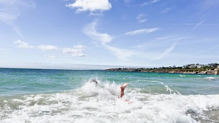 Wall Mural - Handsome boy run and jump into ocean wave on the sand beach