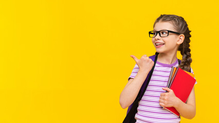 A little joyful girl holds notebooks in her hand and points to the side at your advertisement.