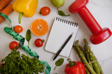 Wall Mural - Notepad, dumbbell, vegetables and fruits on a light background