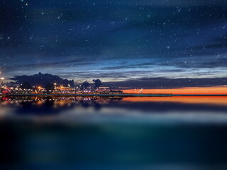 Wall Mural - night sea water blurred city light,blue water wave reflection starry sky and moon in italy port harb