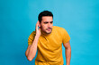 © The Attico Studio - Young bearded male in yellow shirt touching the ear listening while standing against blue background