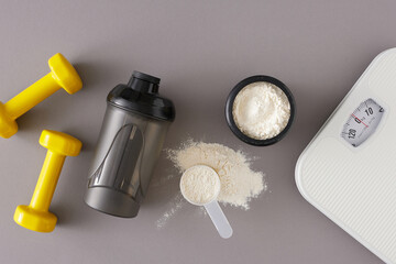 Wall Mural - Gym diet nutrition concept. Flat lay photo of protein powder in jar with shaker, scoop, dumbbells and scales on grey background. Fitness diet idea.