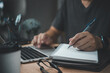© khunkornStudio - man hands with pen writing on notebook in the office.learning, education and work.writes goals, plans, make to do and wish list on desk.