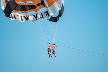 Side, Turkey. October 10, 2022. Low angle view of carefree female friends parasailing in mid-air and enjoying vacation with clear blue sky in the background during sunny day