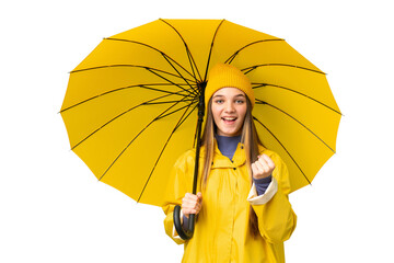 Poster - Teenager girl with rainproof coat and umbrella over isolated chroma key background celebrating a victory in winner position