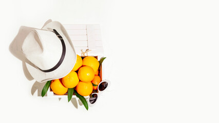 Wall Mural - Summer season fruit card with ripe oranges in wooden box with summer hat and sunglasses on white background, copy space. Healthy vegan or vegetarian food. Harvesting and eco friendly products concept