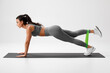 © nikolas_jkd - Athletic girl doing exercise for glutes with resistance band on gray background. Fitness woman working out