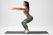 © nikolas_jkd - Athletic girl doing squats exercise for glute with resistance band on gray background. Fitness woman working out