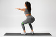 © nikolas_jkd - Athletic girl doing squats exercise for glute with resistance band on gray background. Fitness woman working out