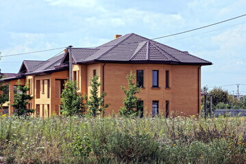 Wall Mural - one large private red brick house under a brown tiled roof stands in green grass on the street against the sky