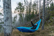 © oleksandr - Man taking a selfie on a smartphone while lying in a hammock in the woods.