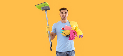 Poster - Happy young man with cleaning supplies on yellow background