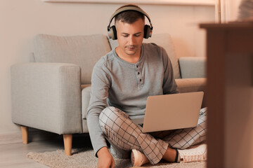 Poster - Young man with headphones and laptop studying online at home late in evening