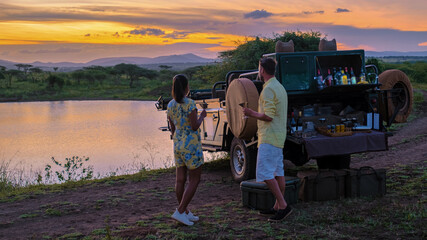 A couple of men and an Asian woman on safari in South Africa, a luxury safari car during a game drive, couple men and woman on safari in South Africa at sunset sundowner with cocktails and drinks