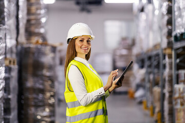 Wall Mural - Portrait of a smiling female controller standing in factory warehouse and using tablet.