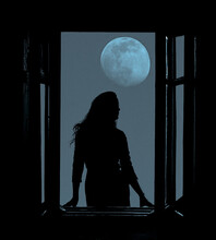 Full Moon In The Night Dark Blue Sky. Black Silhouette Of  Magical Witch Woman Looking Out Of An Open Balcony Window. Evening Heaven Background. Insomnia Idea, Concept. Young Pretty Lunatic Girl.