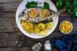 Roast sea bream with potatoes and vegetables on wooden table
