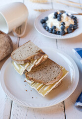 Wall Mural - Healthy breakfast sandwich with sourdough bread and quark cheese. Served with a fresh yogurt and berries on white background 