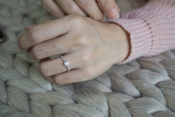 Wall Mural - Close up of an elegant engagement diamond ring on woman finger with pink sweater winter clothe. love and wedding concept. Soft and selective focus.