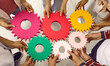 © Studio Romantic - Students or business people joining gears. Team of men and women standing in circle and holding colorful cogs. Cropped shot. Teamwork, integration, business, education, success concept background