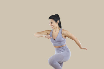 Wall Mural - Happy sporty woman in lilac sports bra and leggings enjoying her gym workout. Joyful fit middle aged lady in comfortable sportswear smiling and doing fitness exercise isolated on beige background