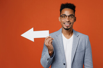 Young happy fun smiling employee business man corporate lawyer wearing classic formal grey suit shirt glasses working in office showing aside with arrow isolated on plain red orange background studio.