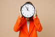 © ViDi Studio - Young successful employee business woman corporate lawyer wear classic formal orange suit glasses work in office hold cover hiding face with clock show time isolated on plain beige background studio.