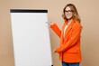 © ViDi Studio - Young smling successful employee business woman corporate lawyer 30s wear classic formal orange suit glasses work in office show flipchart marker board graph isolated on plain beige background studio