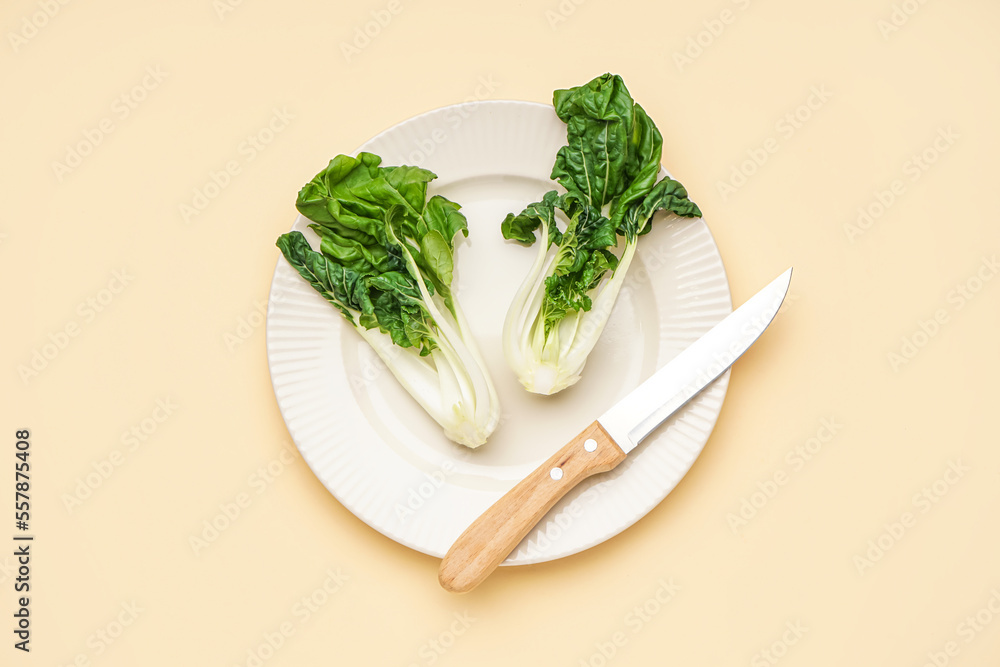 Plate of fresh pak choi cabbage and knife on color background