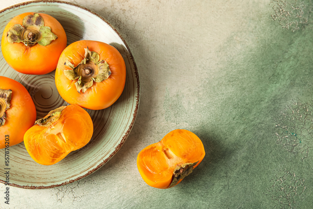Plate with fresh persimmons on grunge background