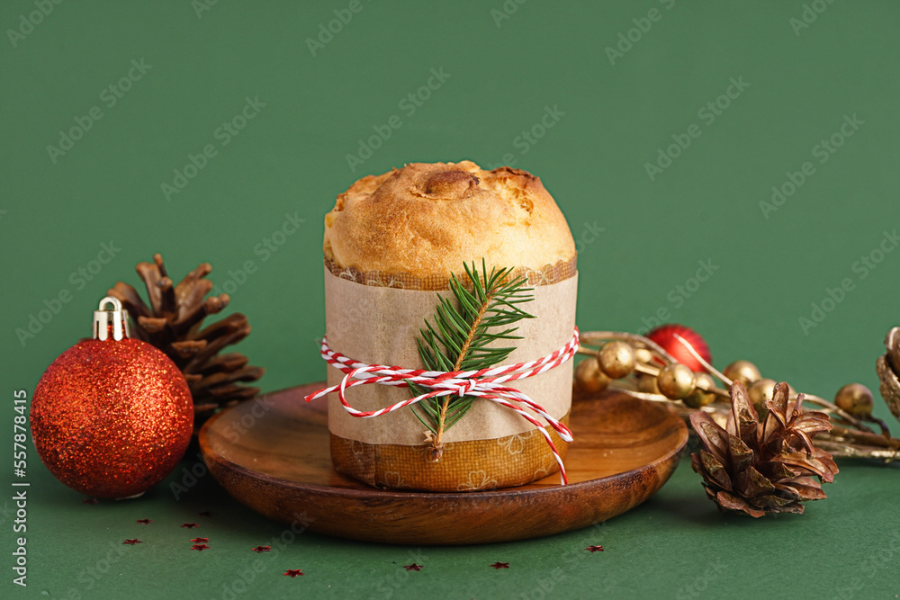 Plate with tasty Panettone and Christmas decor on green background